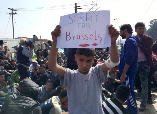 A refugee boy holds up placard reading "Sorry for Brussels" as refugees and migrants take part in a protest against the closure of the border at Greek-Macedonian