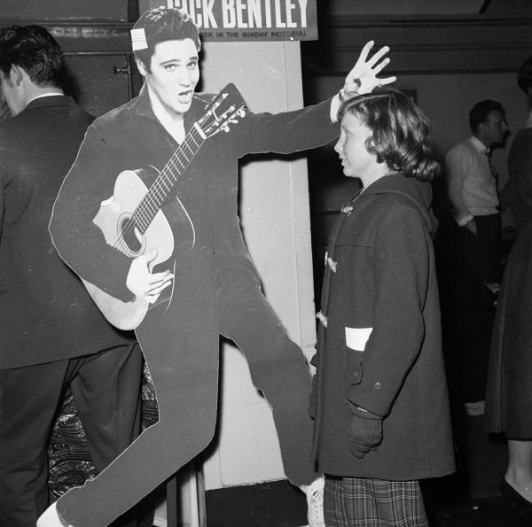 February 1958: 18 year old Elvis fan Lillie Cooper of Tollworth in Surrey staring at a life-size cardboard cut-out of Elvis Presley, a prize in a raffle to be drawn at the rock 'n' roll contest at Wimbledon Palais in London. (Photo by Rosemary Matthews/BIPs/Getty Images)