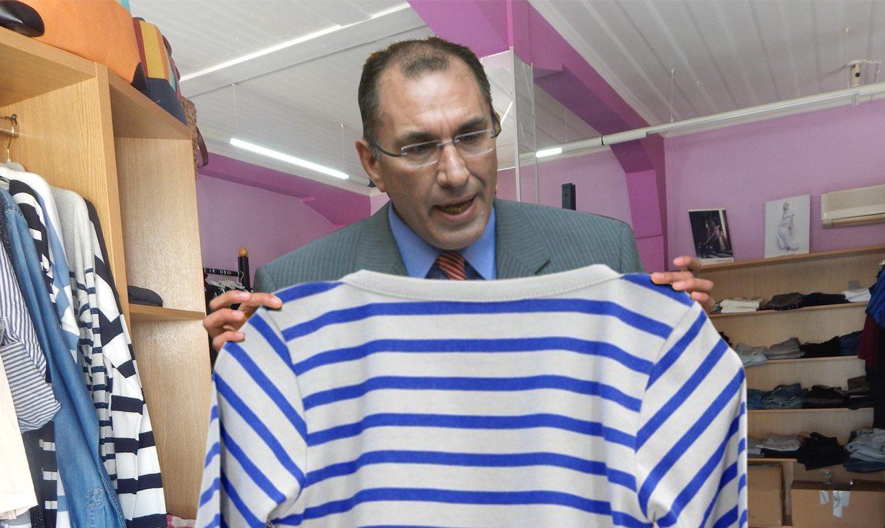 Ο Δημήτρης Καμμένος επιδεικνύει στον φακό το σοκαριστικό αποτέλεσμα της έρευνάς του: μια γαλανόλευκη μπλούζα χωρίς σταυρό!