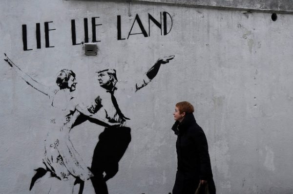 A woman reacts as she walks past a wall mural depicting U.S. President Donald Trump dancing with British Prime Minister Theresa May in London, Britain February 18, 2017. REUTERS/Toby Melville FOR EDITORIAL USE ONLY. NO RESALES. NO ARCHIVES.