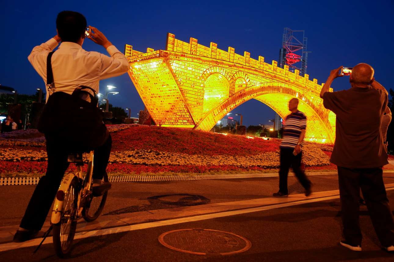 Περαστικοί απαθανατίζουν την εικαστική εγκατάσταση «Χρυσή γέφυρα στον δρόμο του μεταξιού» που έχει στηθεί με αφορμή το συνέδριο Belt and Road, στο Πεκίνο (REUTERS/Thomas Peter)