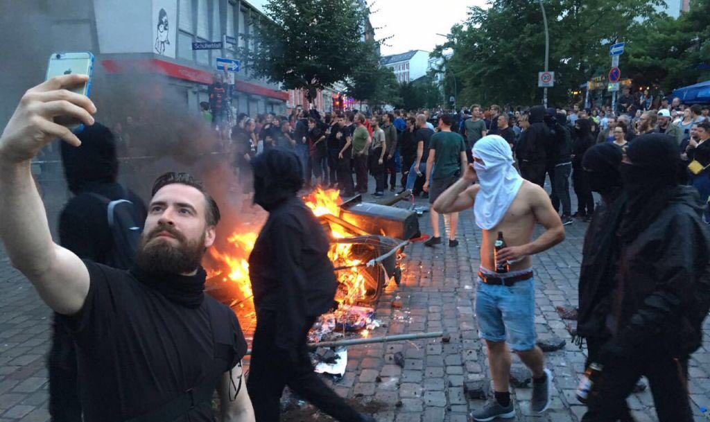 Η φωτογραφία που κάνει τον γύρο του Διαδικτύου. Διαδηλωτής εμφανίζεται σε σέλφι πόζα με φόντο φωτιές του «μαύρου μπλοκ». Ενας αντικαπιταλιστής, ένας πολέμιος της παγκοσμιοποίησης, στον κόσμο της Apple και του Instagram;