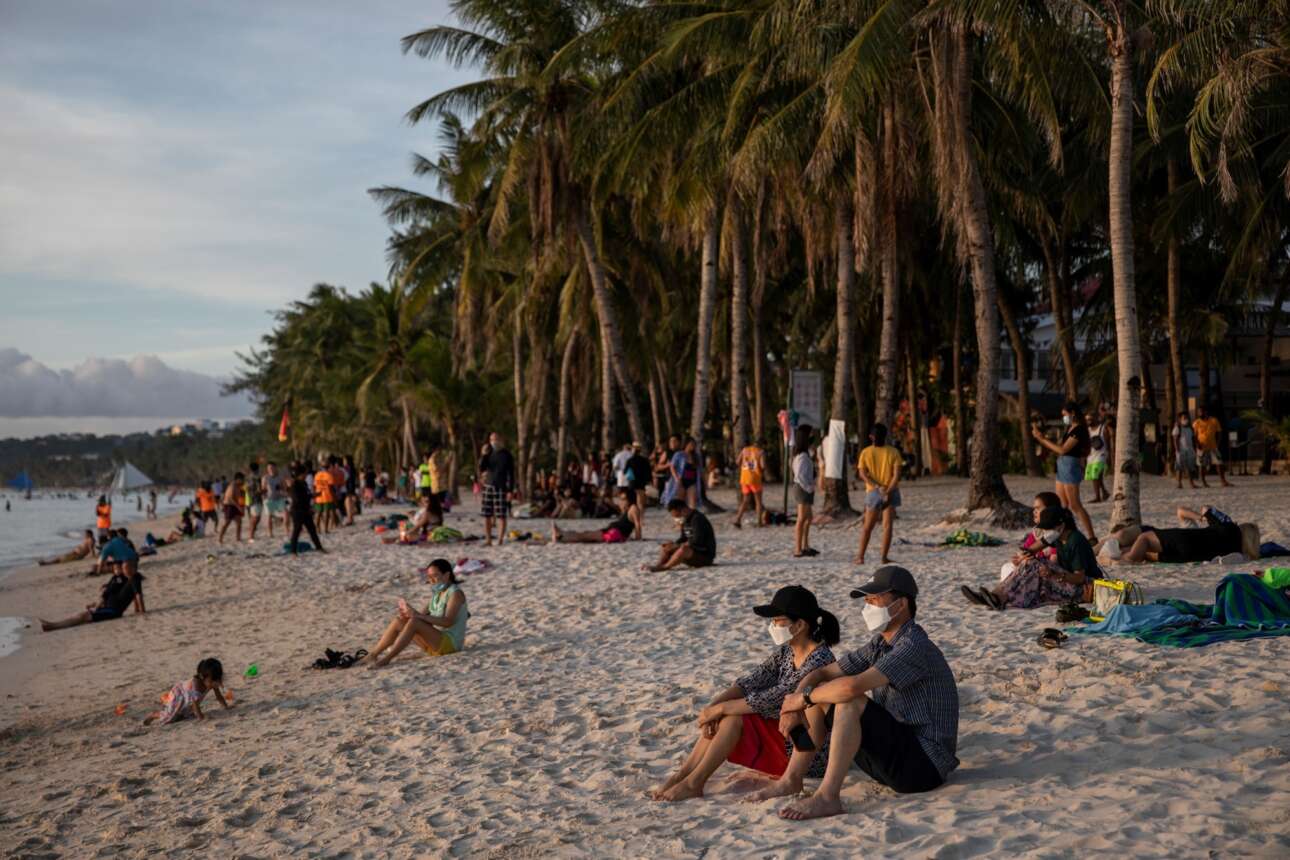 Πολύ μακριά από το Νησί και την Ευρώπη, στις Φιλιππίνες, ο κόσμος συρρέει στις παραλίες φορώντας μισό κομμάτι ύφασμα για ρούχα και ξαπλώνει στην άμμο, κάτω από τις φοινικιές, φάτσα στο ηλιοβασίλεμα. Ομως και εδώ οι υγειονομικές μάσκες δηλώνουν το πρόβλημα
