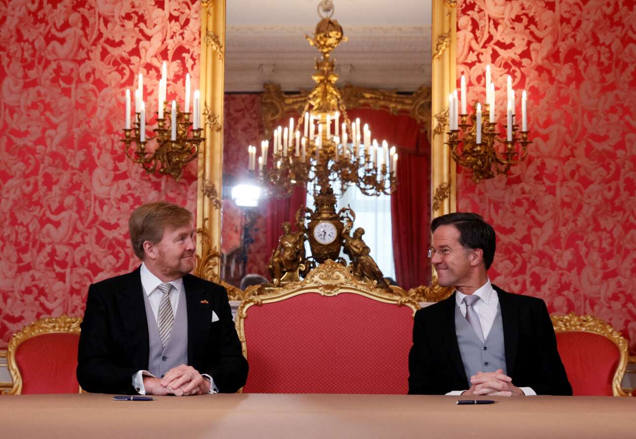 Ο βασιλιάς της Ολλανδίας Βίλεμ-Αλεξάντερ και ο πρωθυπουργός της Μαρκ Ρούτε σε ένα ευτυχισμένο για τον δεύτερο στιγμιότυπο, λίγο πριν από την υπογραφή του διατάγματος περί σχηματισμού κυβερνήσεως – το καρέ προβάλλεται ως ένδειξη σεβασμού στο ενδυματολογικό πρωτόκολλο, που βγήκε αλώβητο από το συντριπτικό χρυσοκόκκινο ντεκόρ της Χάγης 