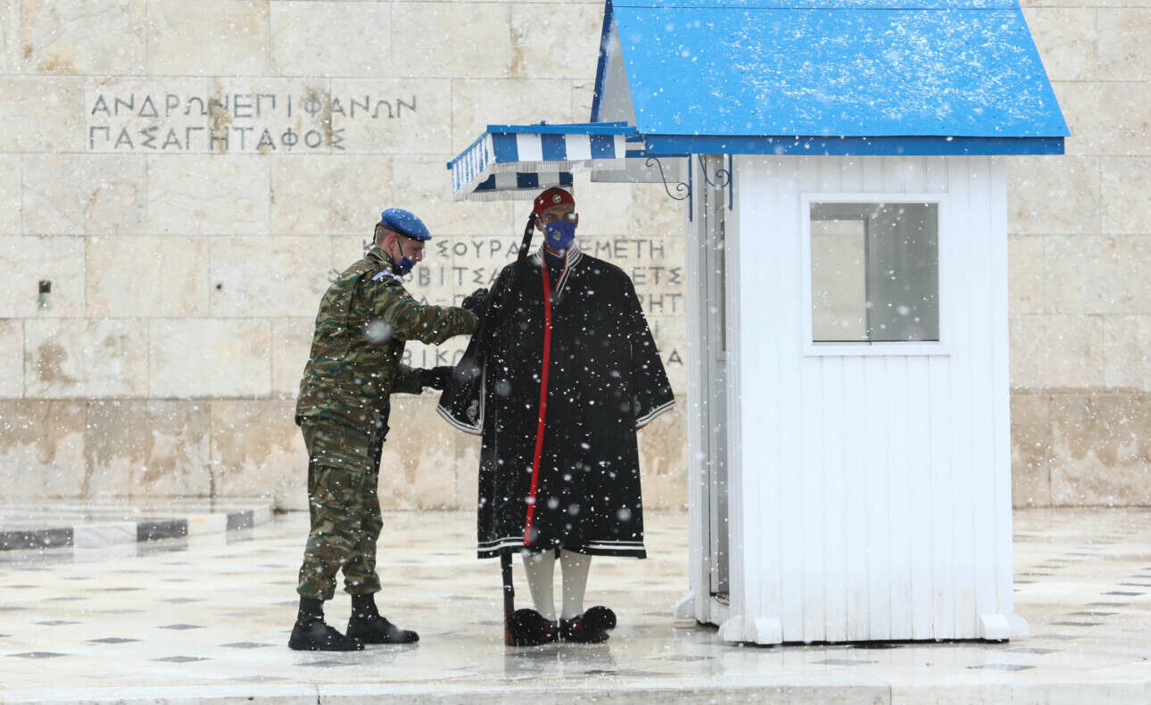 Ανδρας της Προεδρικής Φρουράς ντύνει τον εύζωνα με την υπέροχη χειμερινή κάπα, στο μνημείο του Αγνωστου Στρατιώτη, ενώ το χιόνι ήδη πέφτει πυκνό