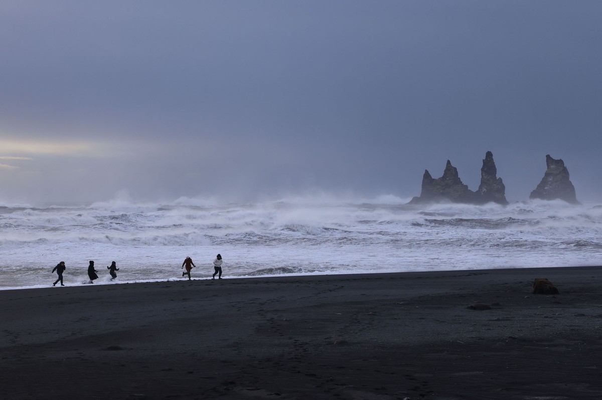 Τουρίστες τρέχουν σε μια παραλία με μαύρη άμμο στο Βικ, στη νότια Ισλανδία, στις 20 Φεβρουαρίου 2022