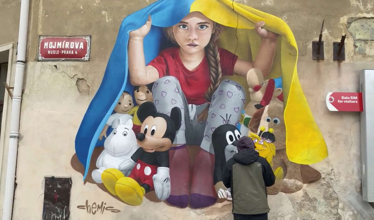 Μία συγκινητική τοιχογραφία στην Πράγα, όπου ένα τρομαγμένο κοριτσάκι κρύβεται κάτω από την ουκρανική σημαία μαζί με τα παιχνίδια της