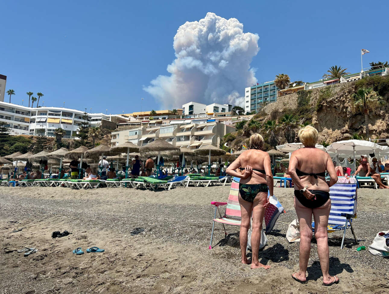 Παραθεριστές κοιτάζουν τα σύννεφα καπνού που προκλήθηκαν από μια πυρκαγιά στη Μάλαγα, καθώς υψώνονται πάνω από την παραλία