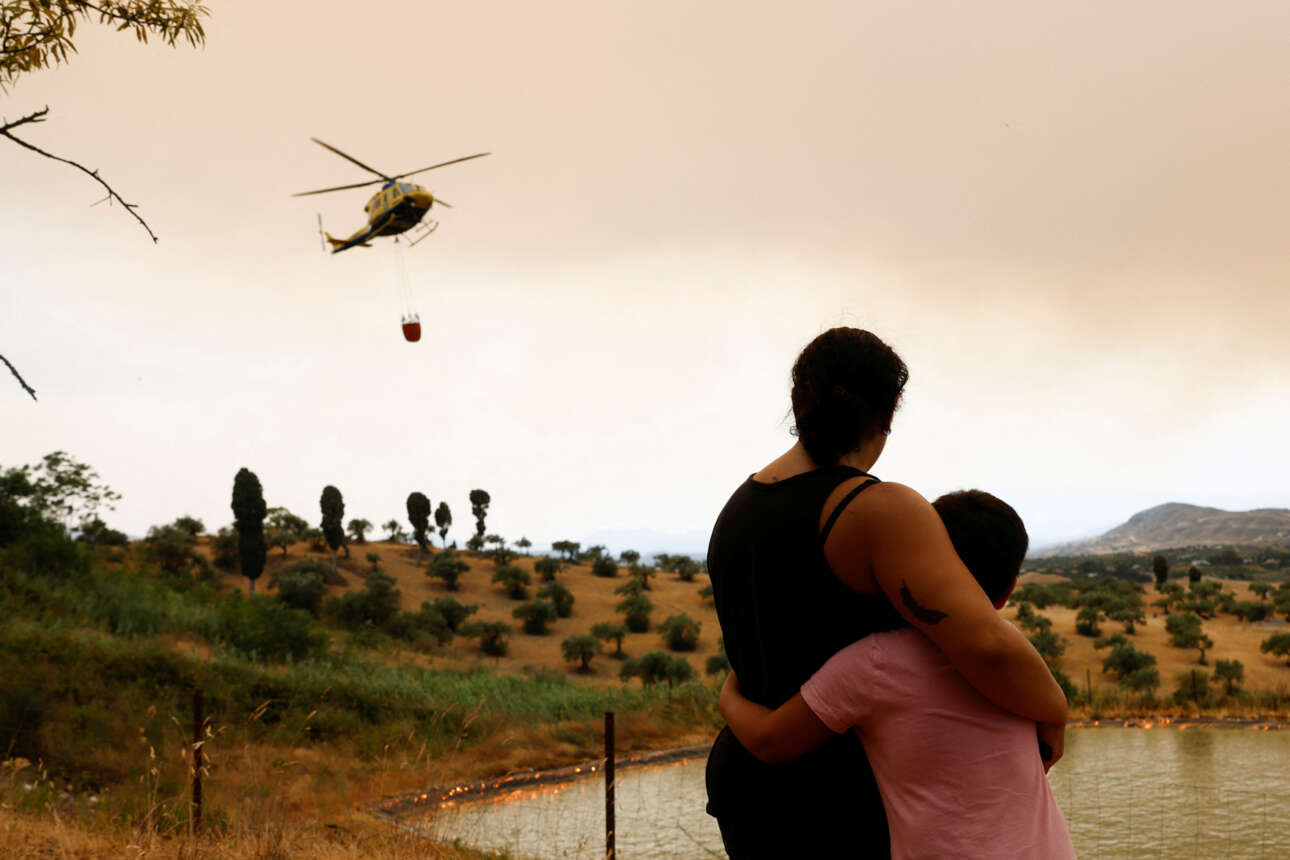 Μάνα και γιος αγκαλιασμένοι και απεγνωσμένοι κοιτάζουν το ελικόπτερο που προσπαθεί να κατασβέσει την πυρκαγιά στο Alhaurin el Grande, στη νότια Ισπανίαμ