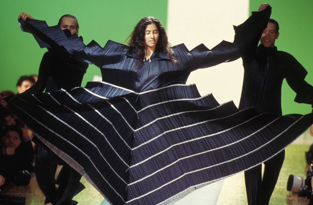 Μοντέλο με χαρακτηριστικό πλισέ ρούχο σε επίδειξη μόδας στο Παρίσι, το 1994. Ο Μιγιάκε ανέπτυξε έναν νέο τρόπο να κάνει πλισέ τα υφάσματα τυλίγοντάς τα ανάμεσα σε στρώματα χαρτιού και περνώντας τα ύστερα από πρέσα θερμότητας. Αρκετές δοκιμές απέδειξαν ότι οι πιέτες παρέμειναν στη θέση τους και δεν ζάρωvαν. H τεχνοτροπία αυτή οδήγησε στη σήμα κατατεθέν σειρά του Pleats, Please (Πιέτες, Παρακαλώ)